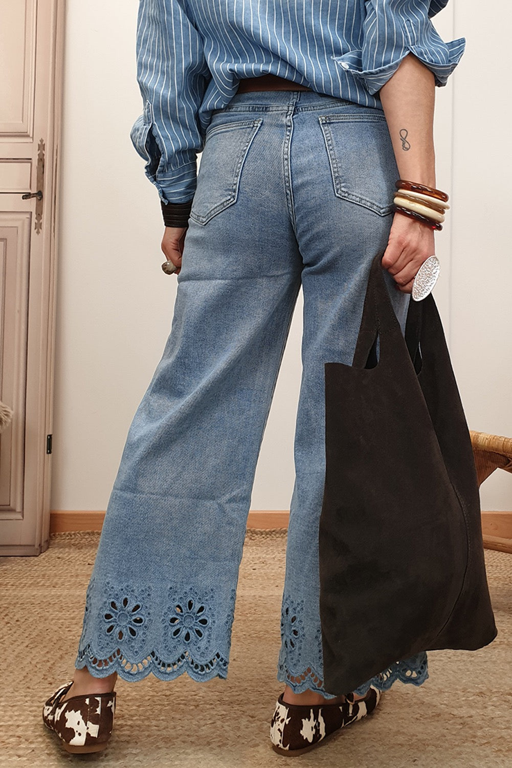 Person wearing blue jeans with lace details and a black bag indoors.