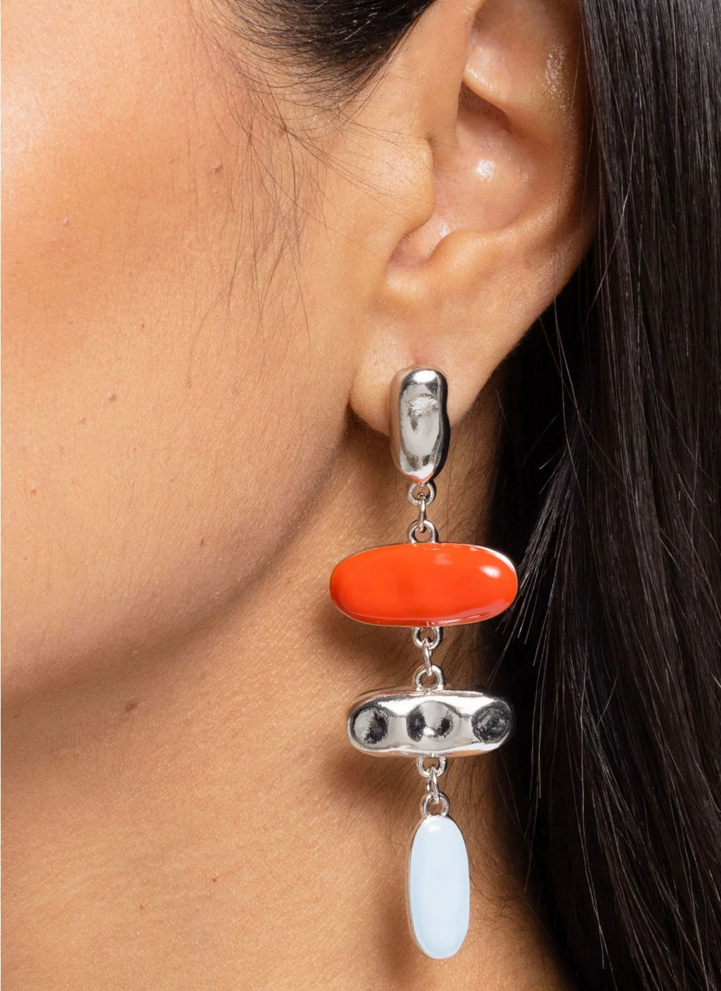 Close-up of an ear wearing a silver earring with orange and white stones.