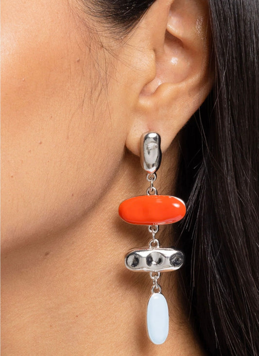 Close-up of an ear wearing a silver earring with orange and white stones.